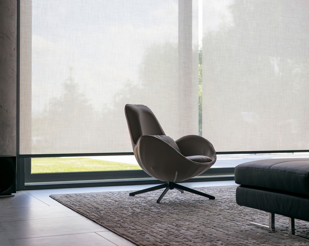 a chair in a room behind is motorised roller blinds.
